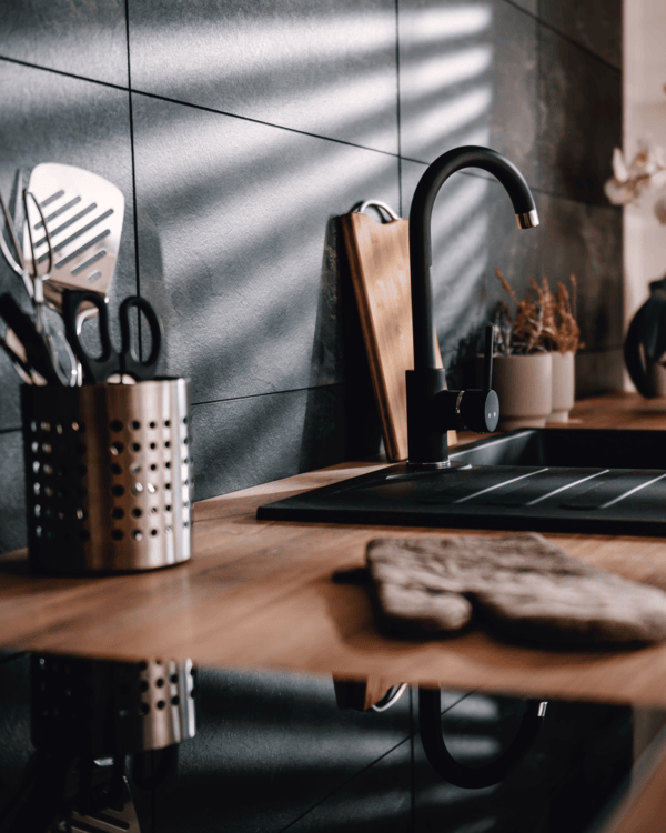 Modern kitchen with wooden countertop, black faucet, and utensils.