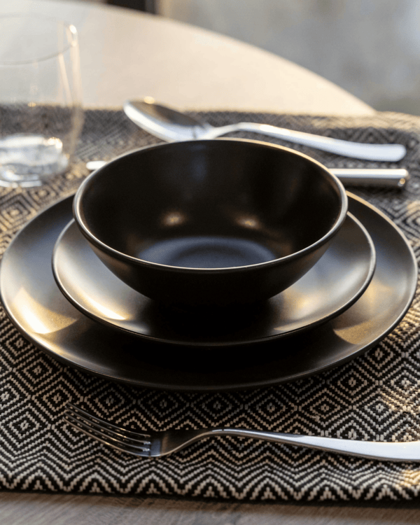 Set of black ceramic plates and bowl on a patterned tablecloth.